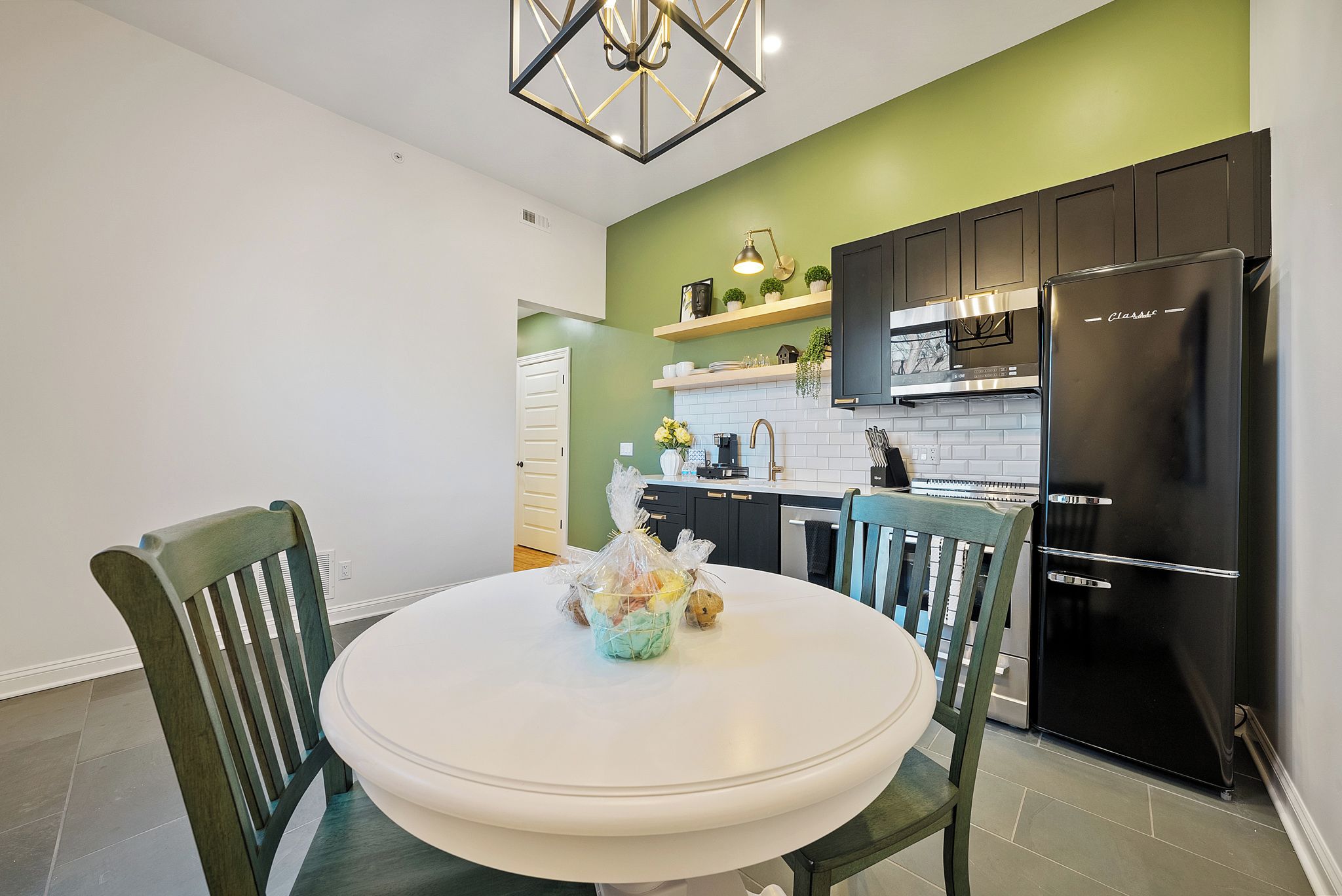 A kitchen with a white table, green chairs, a black refrigerator, and a green accent wall.