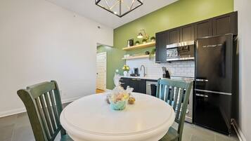 A kitchen with a white table, green chairs, a black refrigerator, and a green accent wall.