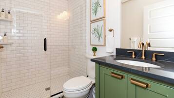 Een badkamer met een witte betegelde douche, een toilet, een wastafel met gouden kraan en groene kastjes.