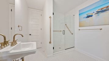 A bathroom with a white sink, a glass shower enclosure, and a painting of boats on the wall.