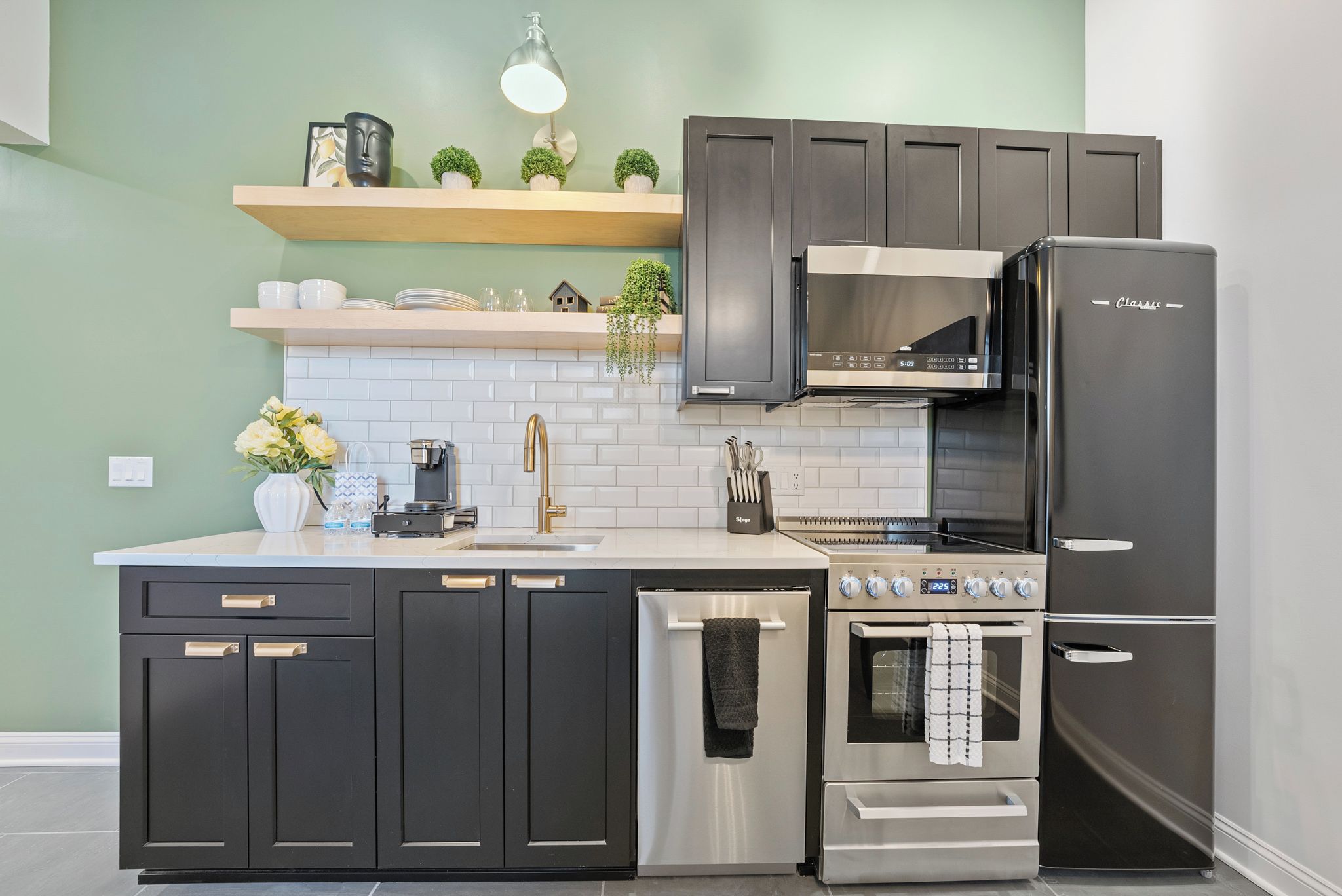 A modern kitchen with dark cabinetry, stainless steel appliances, and a white tiled backsplash.