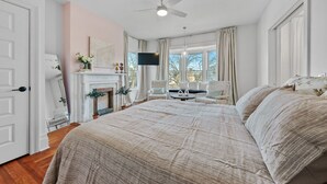 A bedroom with a large bed, a ceiling fan, a fireplace, and a TV. - Elegant Boutique Condo Downtown Sandusky (Sandusky)