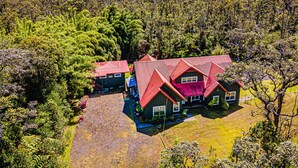 Une grande maison avec un toit rouge, entourée d’une forêt dense.