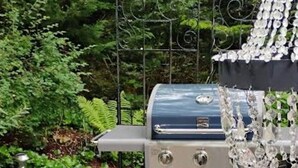 Ein Garten mit Grill, einem Metallstuhl und rosa Blumen in einem Metallkübel.