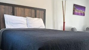 A bedroom with a bed, a headboard, an air conditioning unit, a vase, and a wall-mounted picture. - Adorable studio guesthouse in Hour Glass district. (Orlando)