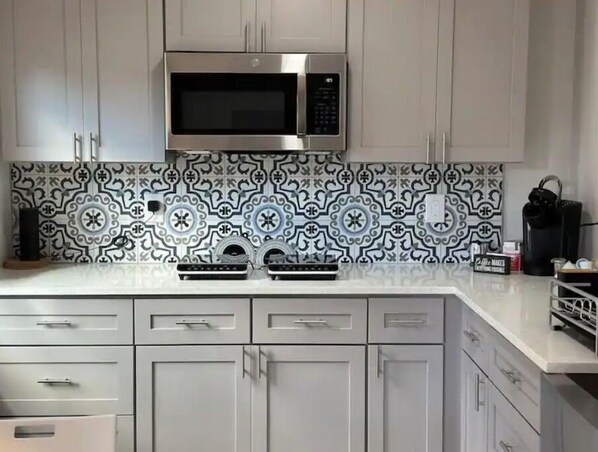 A kitchen with white cabinets, a stainless steel microwave, and patterned backsplash tiles.