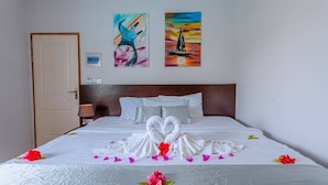 A hotel room with a bed, two paintings on the wall, and a heart-shaped towel arrangement on the bed. - VIOLET INN (Dharavandhoo)