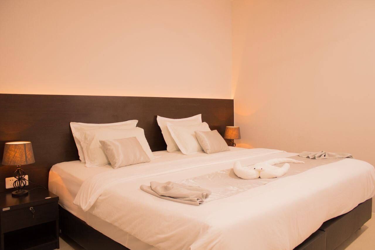A neatly made bed with white linens and pillows, a bedside lamp, and a towel and two swans on the bed.