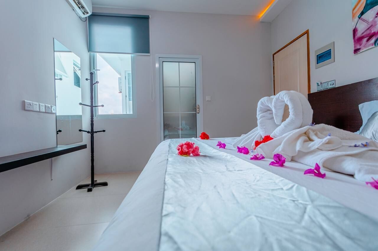 A hotel room with a bed, a bedside table, a mirror, a window, and a door.