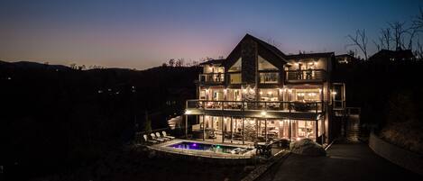 A large, multi-story house with a swimming pool, surrounded by a fence and a rocky landscape.