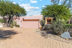 Stroll through the landscaped garden, featuring desert plants and a paved driveway, to the modern single-story home with a flat roof.