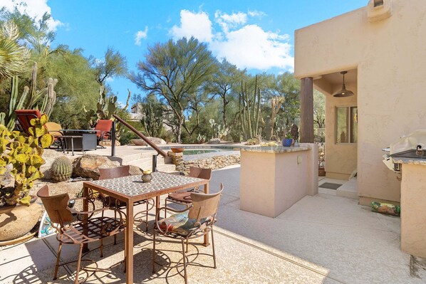 Un patio exterior con mesa y sillas, una parrilla y una zona de piscina.