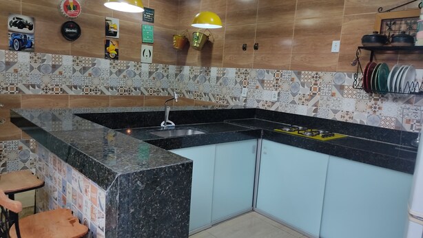 Une cuisine dotée d’un plan de travail en granit, d’un évier et d’une cuisinière. Le mur derrière l’évier est décoré de carreaux et un luminaire suspendu jaune est fixé au-dessus du plan de travail.