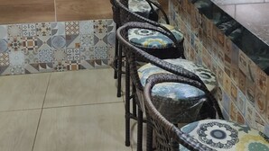 Une cuisine avec un mur recouvert de carreaux, un coin bar avec des chaises en osier et des suspensions jaunes.