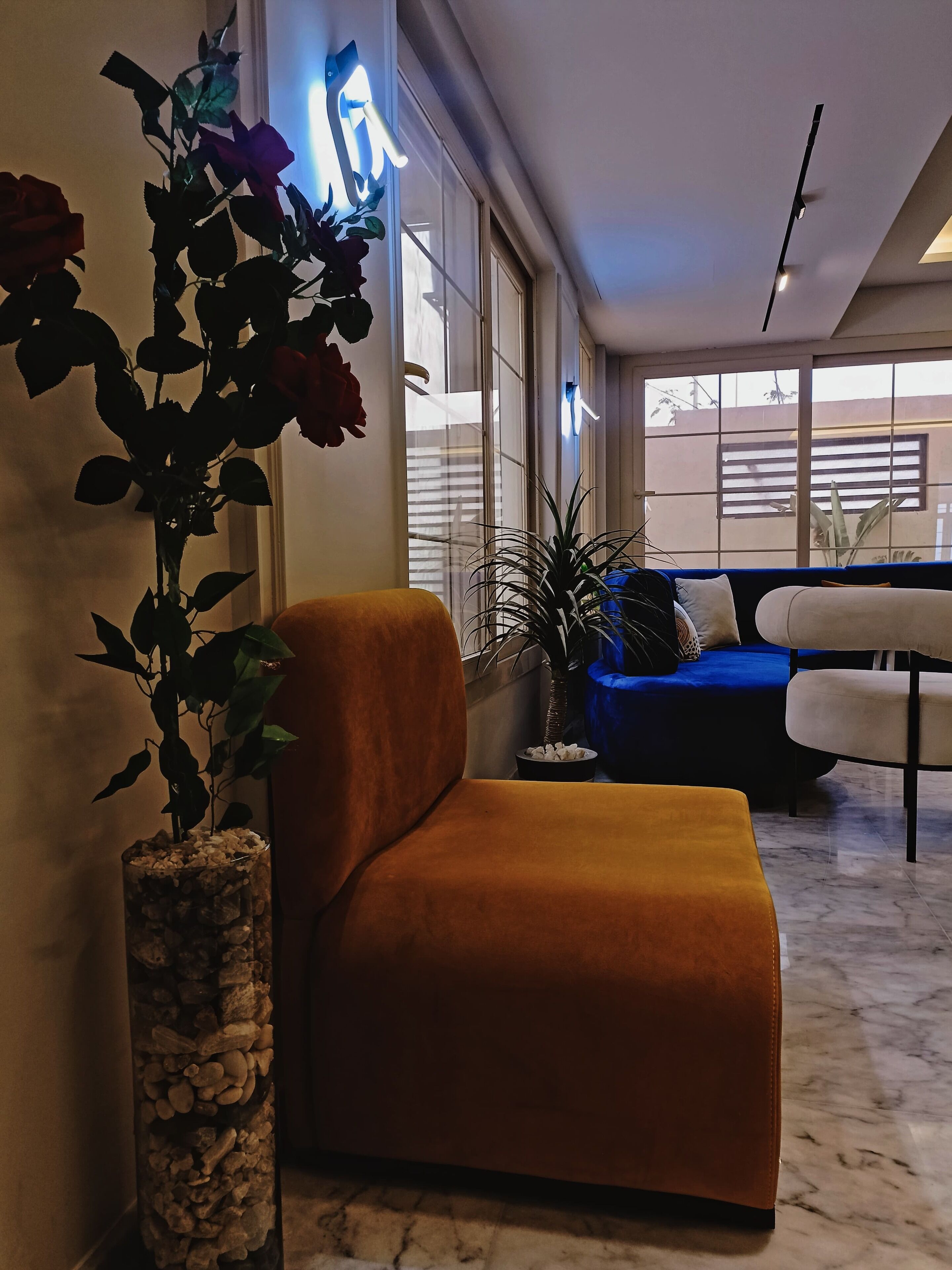A modern living room with a plush orange armchair, a blue sofa, and a potted plant.