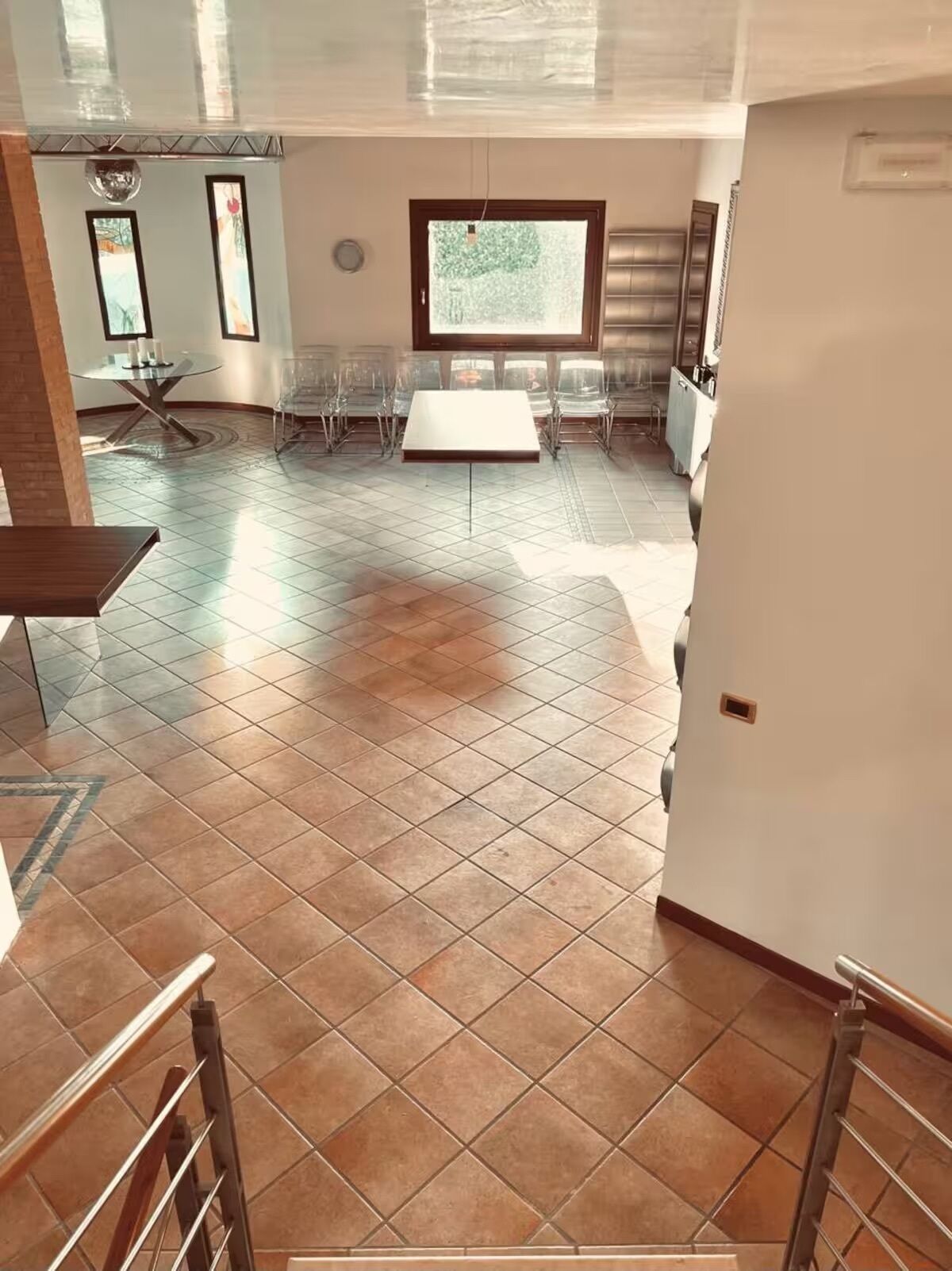 Ein geräumiges Zimmer mit Fliesenboden, einem großen Fenster und einem Essbereich mit klaren Stühlen und einem Tisch.