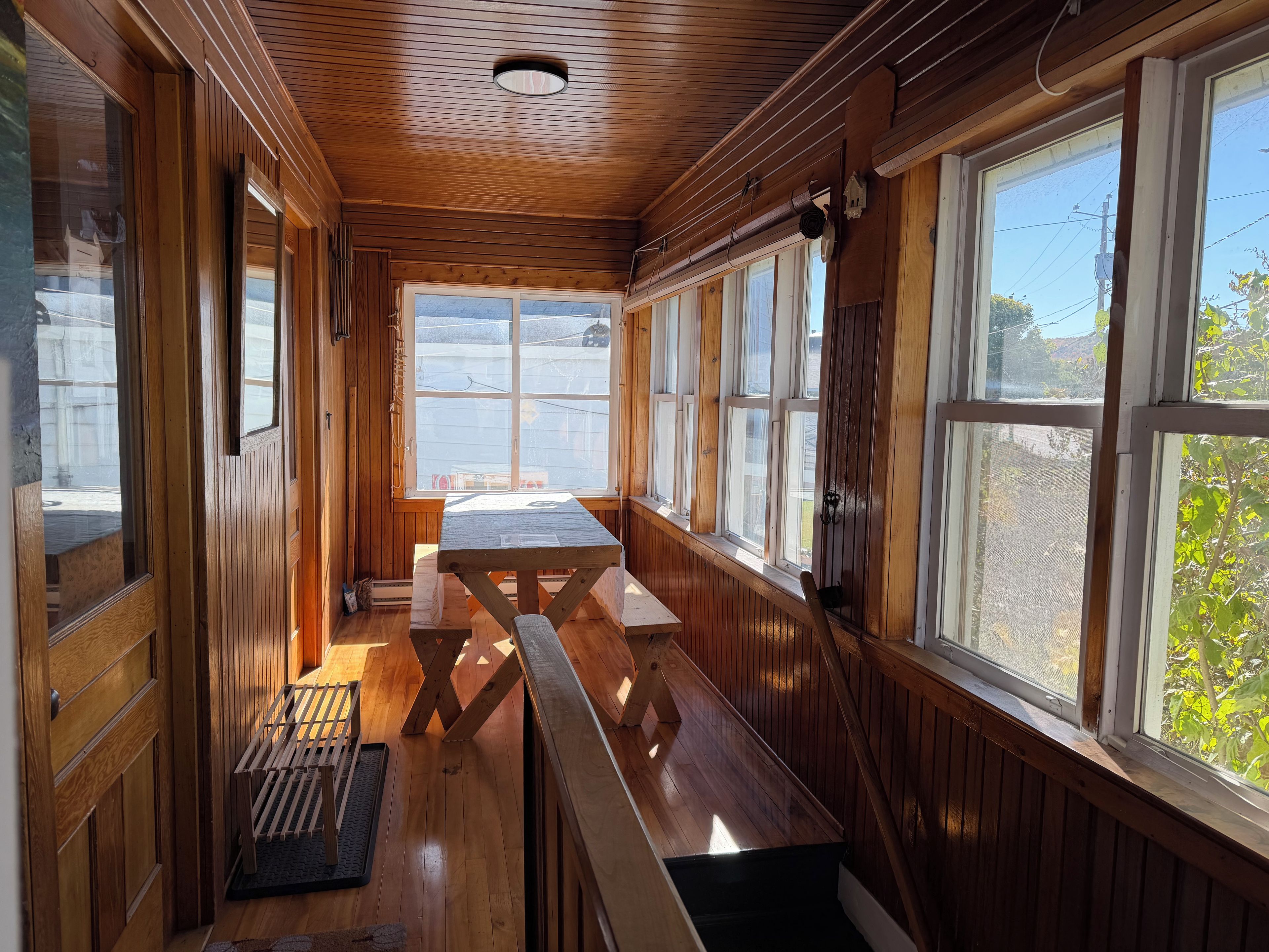 Interior d'una cabana de fusta amb una banca, finestres grans i una làmpada al sostre.