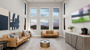 A spacious living room with a large window, a sofa, a coffee table, and a TV on a wooden cabinet. - Luxury Cabin | Private Indoor Pool, Hot Tub & 3 Scenic Decks (Sevierville)