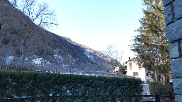 Un bâtiment à la façade en pierre, une clôture en bois et une montagne enneigée en arrière-plan.