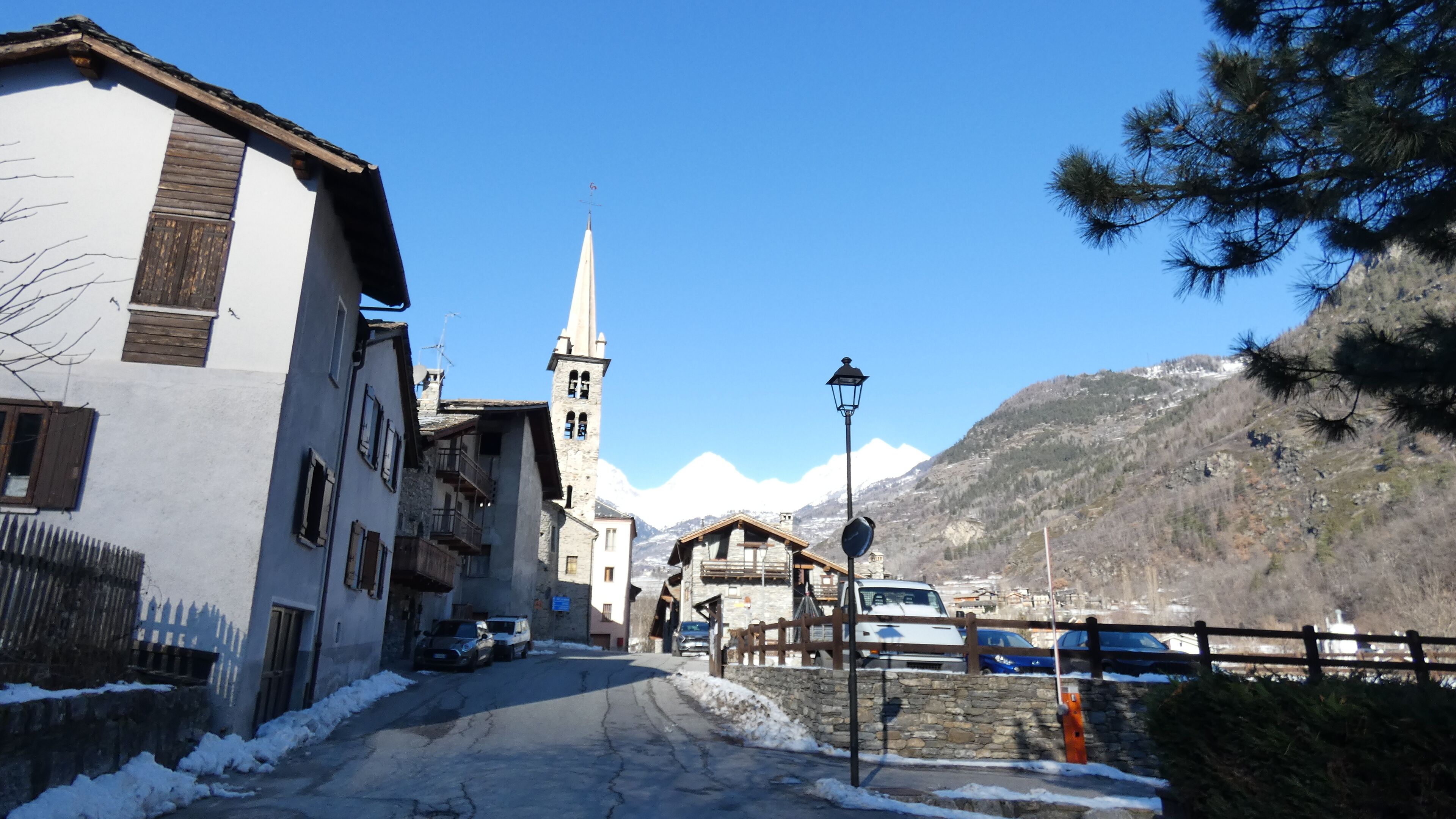 A narrow street with buildings, a church, and a mountain in the background.