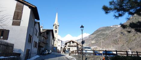A narrow street with buildings, a church, and a mountain in the background.