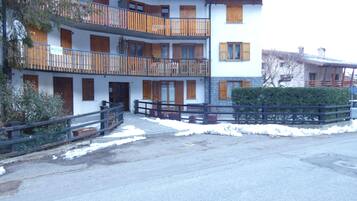 A multi-story building with balconies, a gated entrance, and snow on the ground.