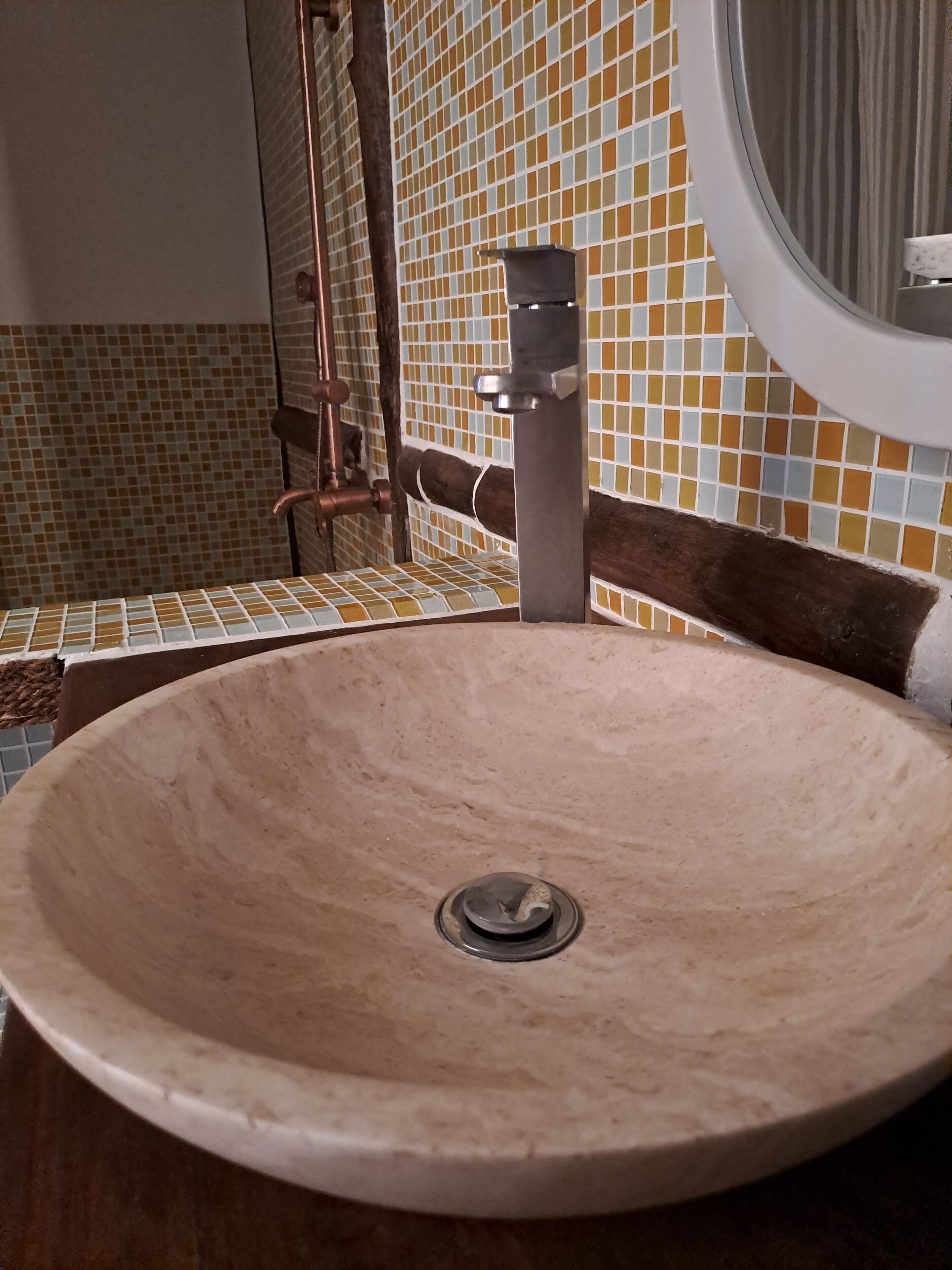 A bathroom with a round sink, a mirror, and tiled walls.