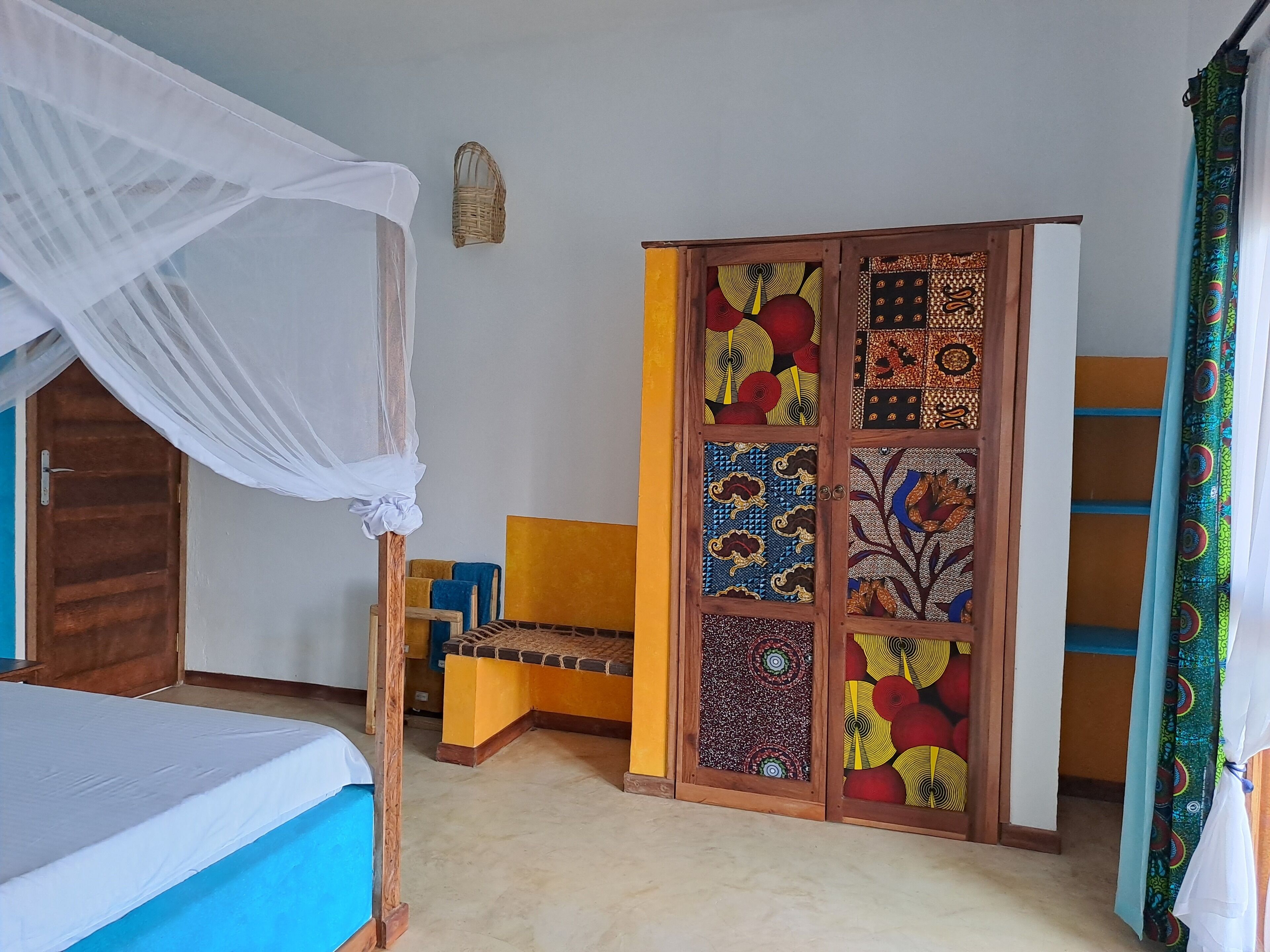 Une chambre à coucher avec un lit, une armoire en bois aux portes à motifs, un banc et une moustiquaire au-dessus du lit.