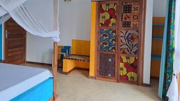 Une chambre à coucher avec un lit, une armoire en bois aux portes à motifs, un banc et une moustiquaire au-dessus du lit.