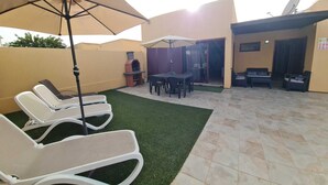A patio with lounge chairs, a barbecue grill, and a dining area with umbrellas.