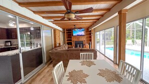 Un espacio habitable amplio con ventilador de techo, chimenea, televisor y vista a una piscina.