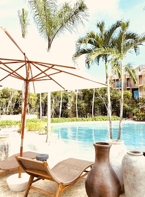 A poolside area with lounge chairs, a large umbrella, and a view of a pool and palm trees.
