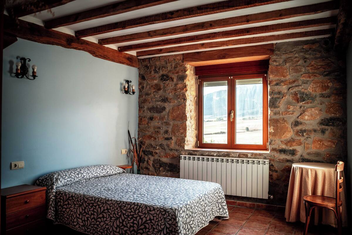 A bedroom with a bed, a window, a radiator, and a wooden ceiling.