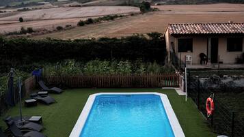 Una piscina rectangular con borde blanco, rodeada de césped artificial y una valla de madera.