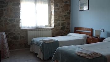 Una habitación con dos camas, una pared de piedra, una ventana con cortinas, un radiador y un cuadro enmarcado en la pared.