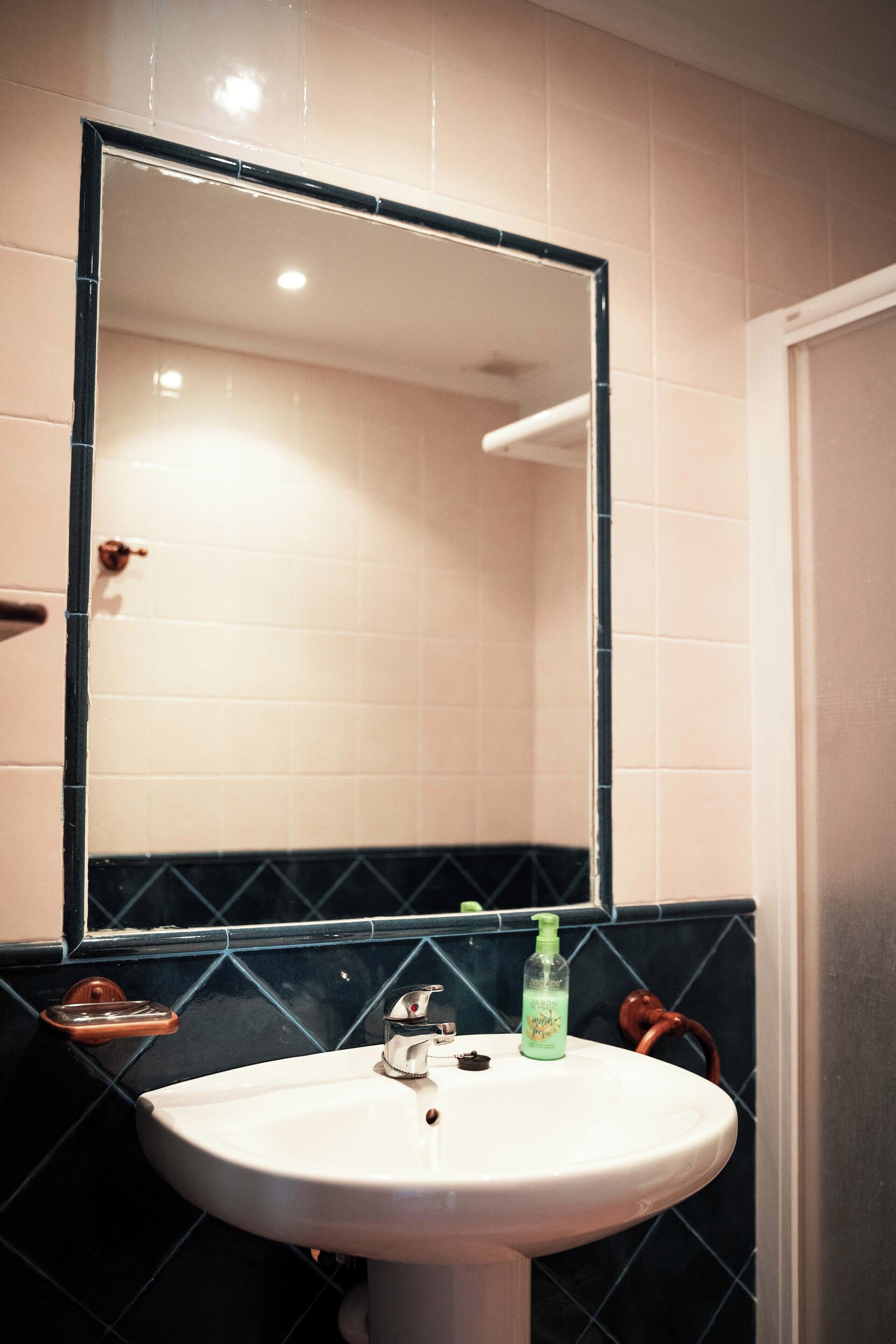 Un baño con un lavamanos blanco, un espejo y un dispensador de jabón verde.