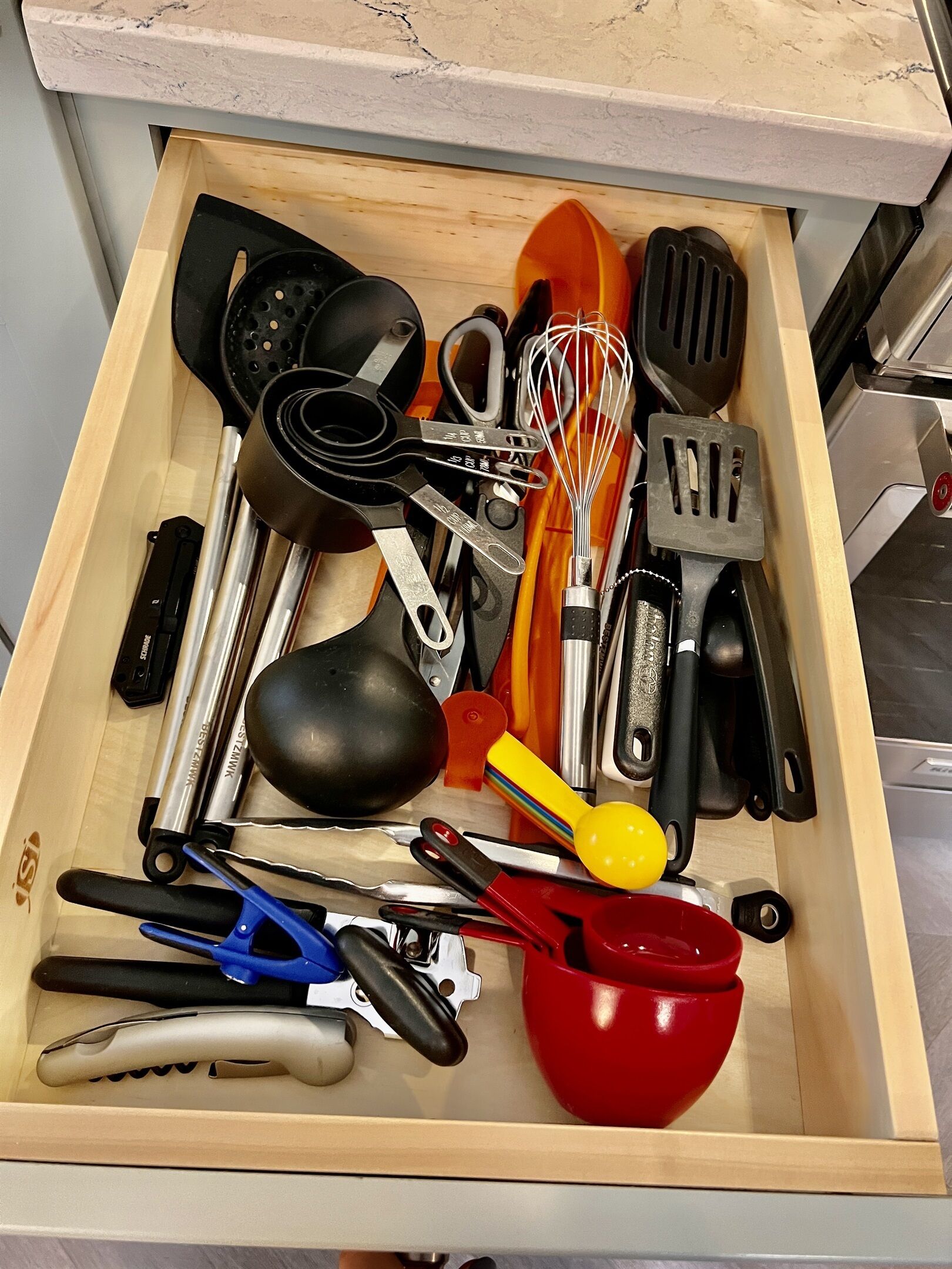 Un tiroir contenant divers ustensiles de cuisine, notamment des spatules, des fouets et des tasses à mesurer.