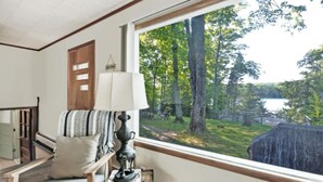A room with a large window overlooking a forest and a lake. There is a chair with a cushion and a lamp on a table. - Summer is here. Great hiking and the falls are beautiful golf courses open (Iron River)