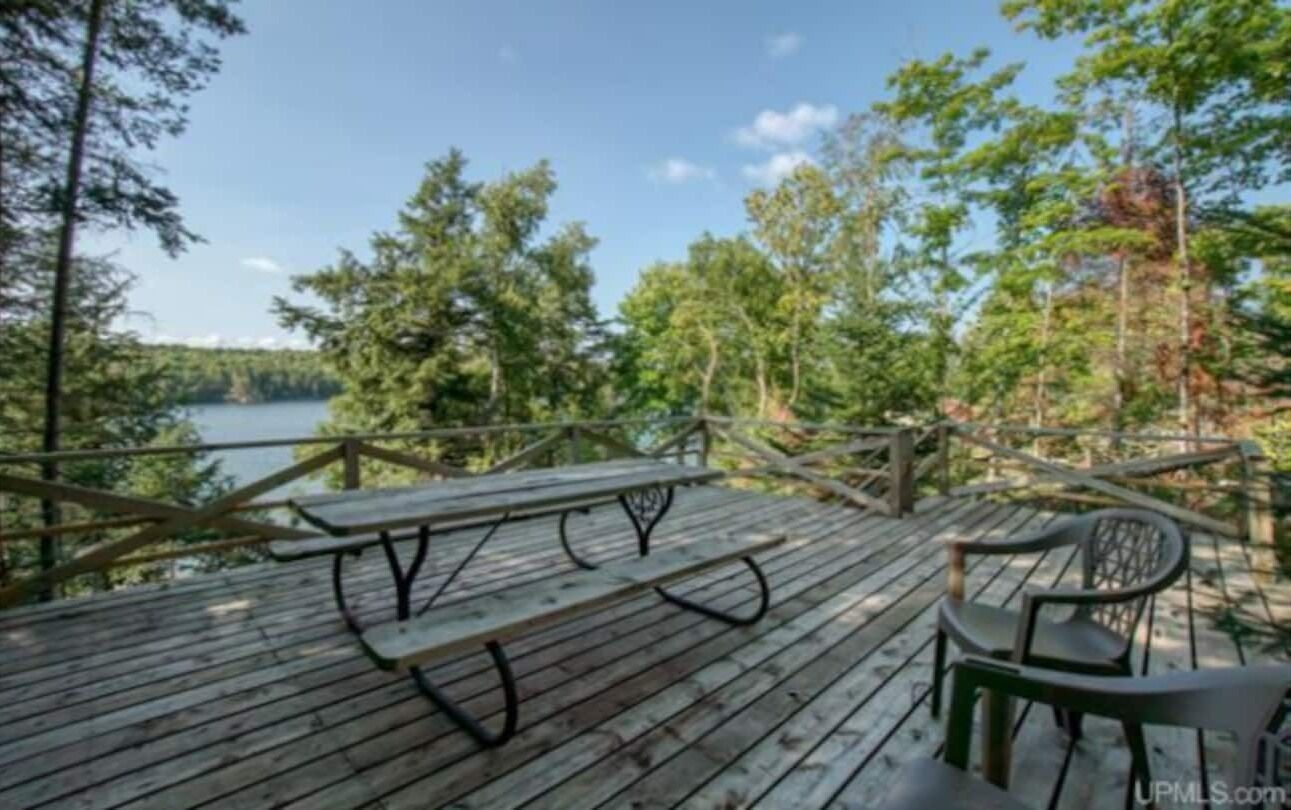 A wooden deck with picnic tables and chairs overlooking a lake surrounded by trees.