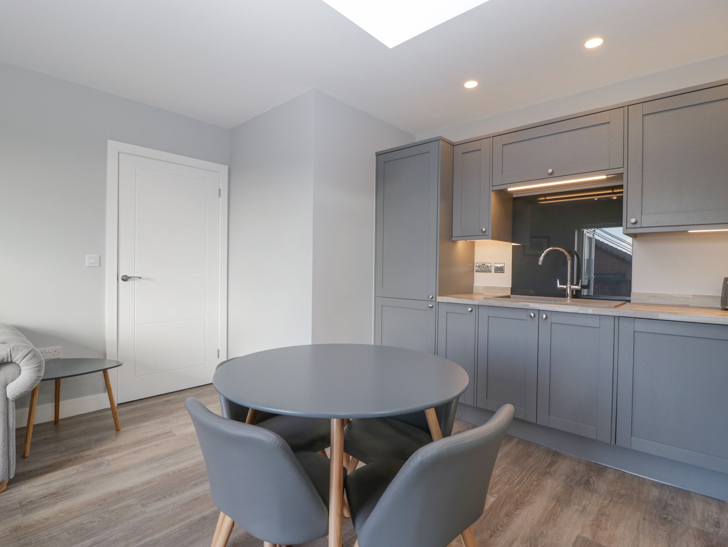A modern kitchen with grey cabinets, a round dining table, and two grey chairs.