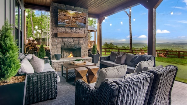 A covered outdoor seating area with stone fireplace, wicker furniture, and a scenic view.