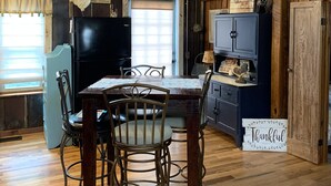 Eine rustikale Küche mit Holzwänden, einem Esstisch mit Stühlen, einem Kühlschrank, einem Fernseher und einem Schild mit der Aufschrift 'Thankful'.