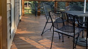Eine Holzterrasse mit Metallstühlen und einem Tisch, umgeben von einem Holgitter und Bäumen.