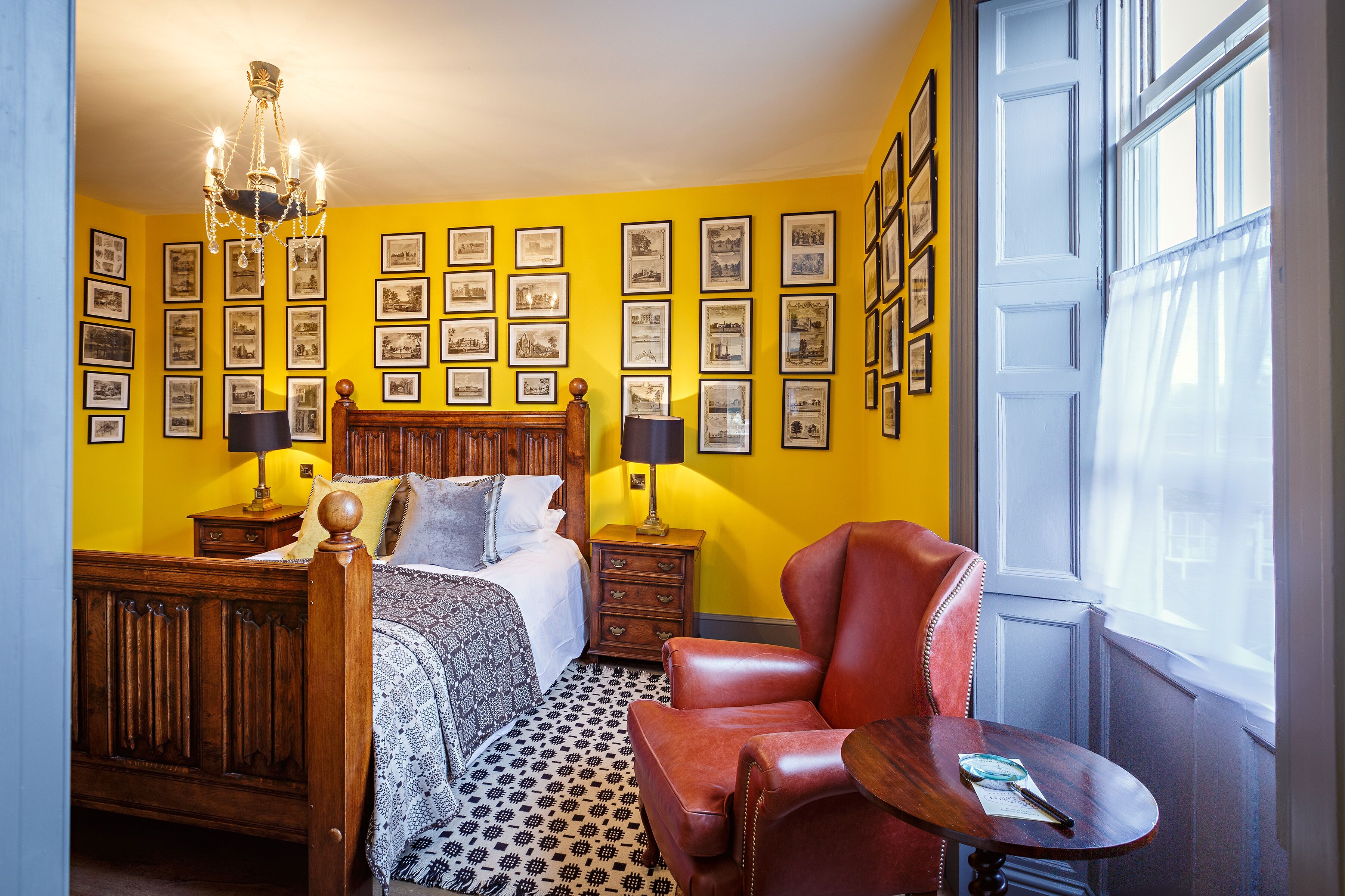 Un dormitorio con una cama de madera, un sillón de cuero rojo, una mesita pequeña y una pared decorada con marcos de fotos.