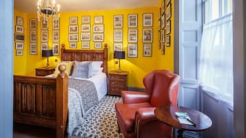 Un dormitorio con una cama de madera, un sillón de cuero rojo, una mesita pequeña y una pared decorada con marcos de fotos.