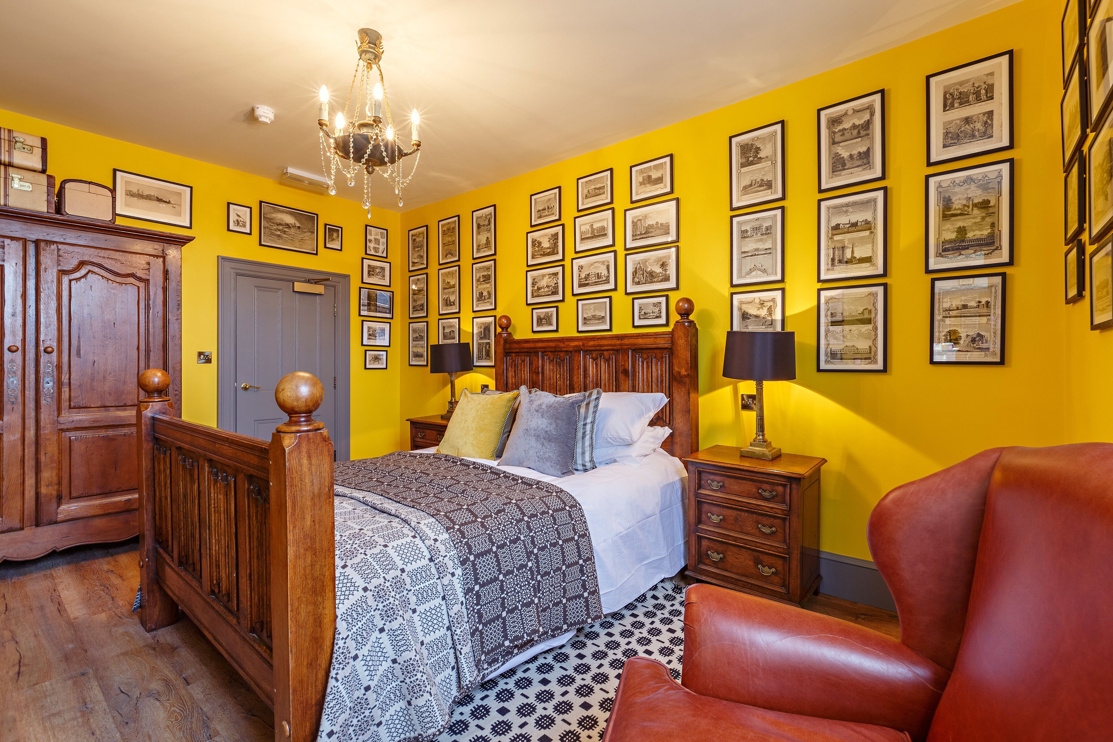 A bedroom with a wooden bed, a red leather chair, a chandelier, and a wall decorated with framed pictures.