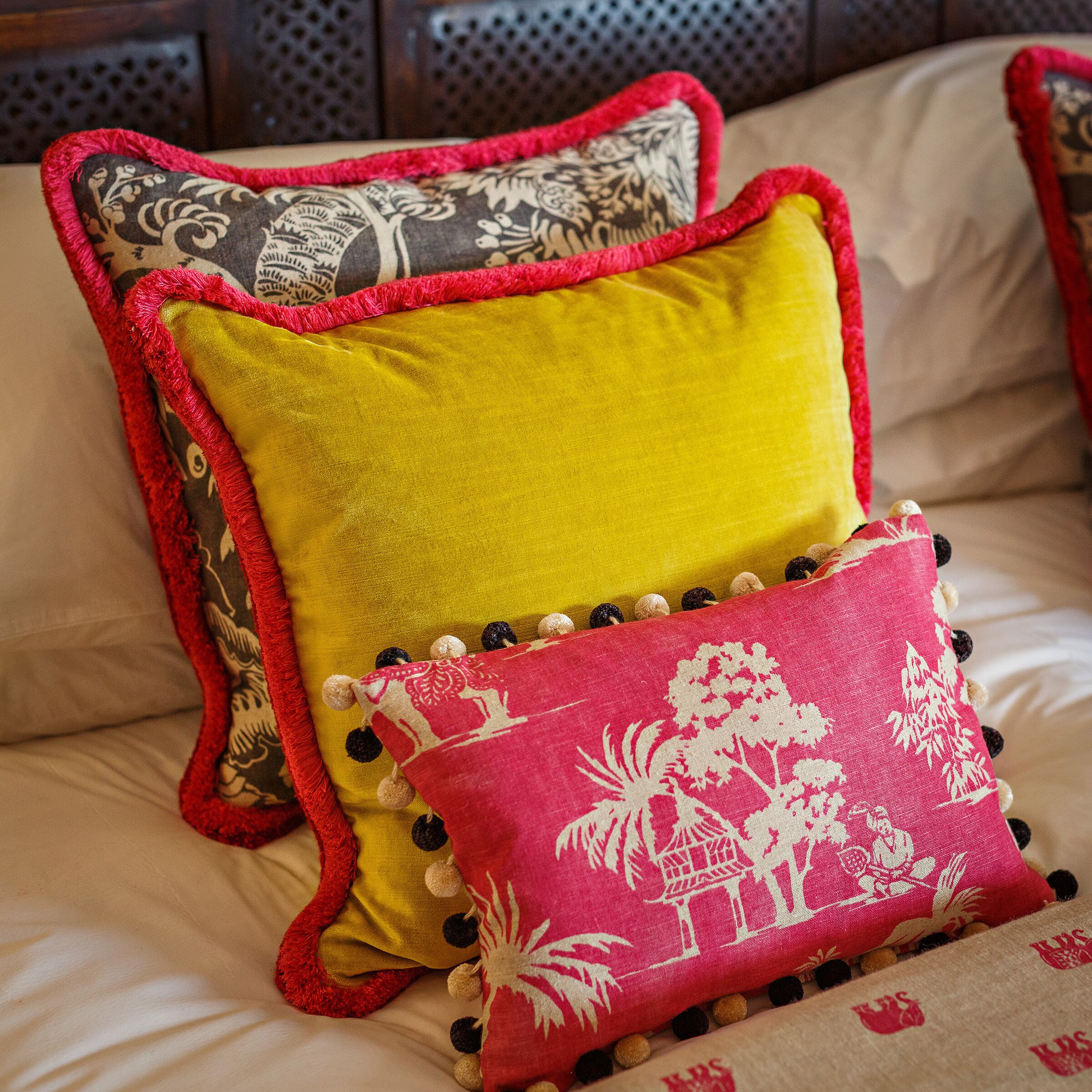 Una cama con tres almohadas: una con estampado floral, una amarilla lisa y otra con diseño tropical.