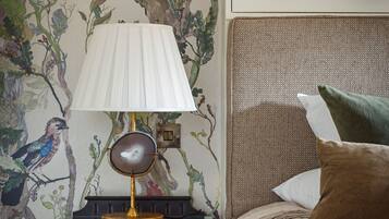 A bedroom with a bed, a nightstand with a lamp, and a wall with a nature-themed mural.