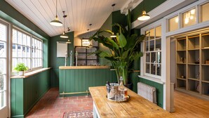 A cozy bar area with a wooden table, green walls, and a large plant. - The Dial House (Norwich)