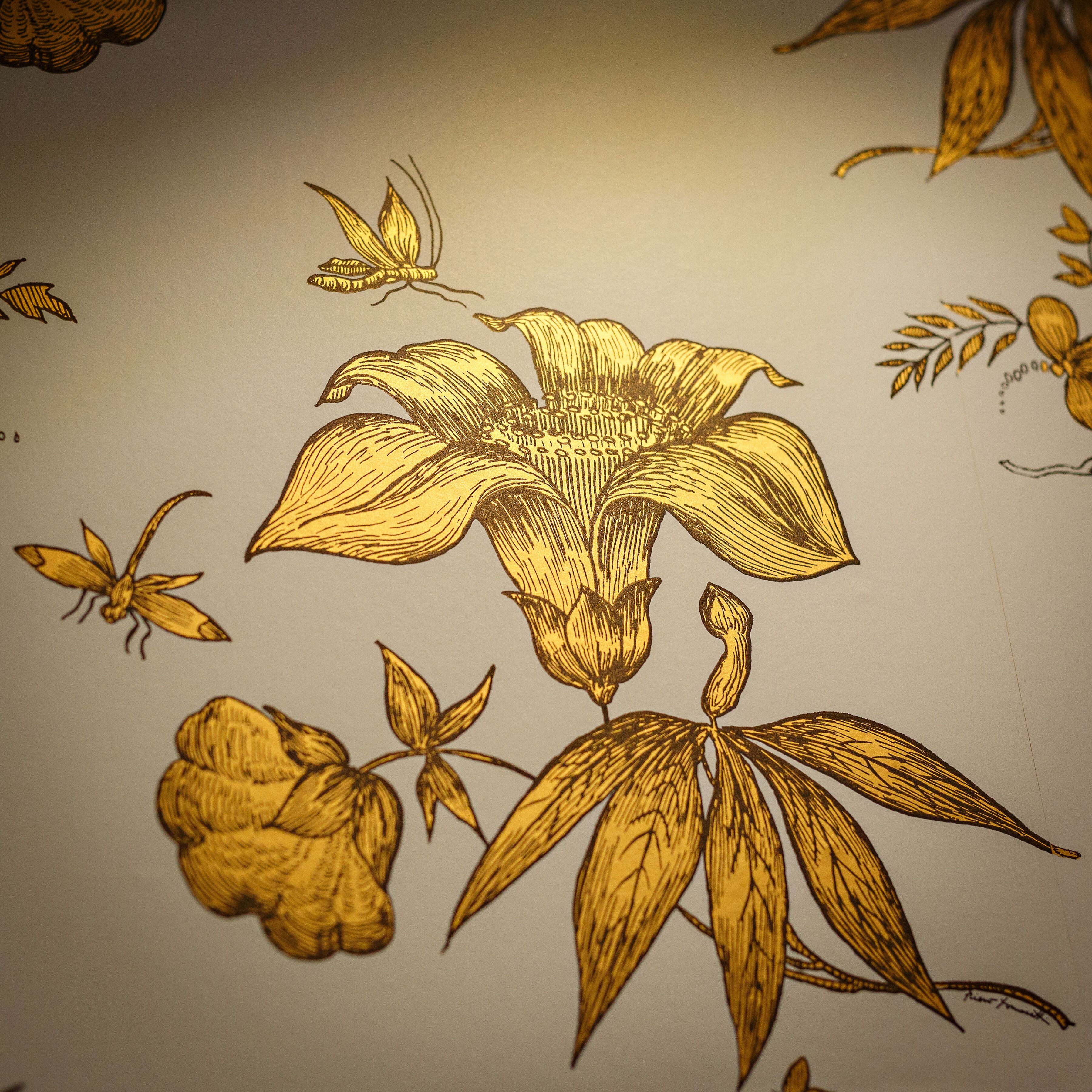 Et nærbillede af tapet med et stort, centralt blomsterdesign og mindre botaniske detaljer.